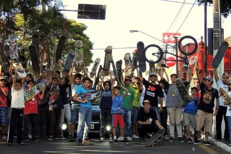Várias pessoas juntas posando em frente a um carro, todas com o skate levantado sobre a cabeça